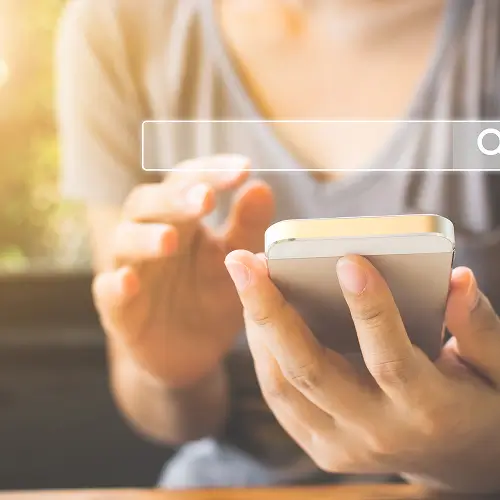 Hands holding a smartphone with digital search bar, emphasizing the user journey to get found online by Elevation Marketing