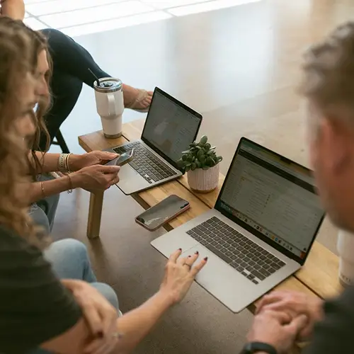 Group of marketers collaborating with laptops and smartphones, working on entity SEO strategies for digital marketing in the age of AI