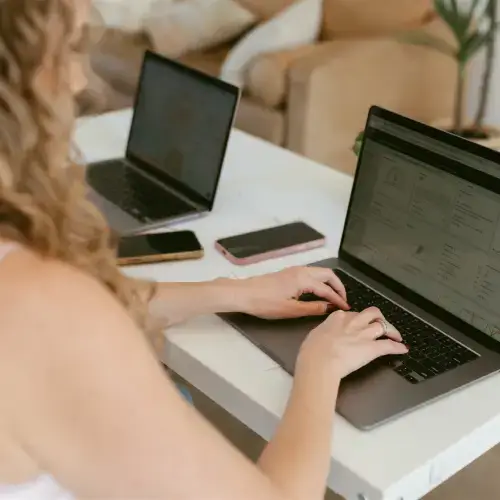 A marketing professional working on contractor marketing strategies at a desk with two laptops, smartphones, and analytics software, representing Elevation Marketing.