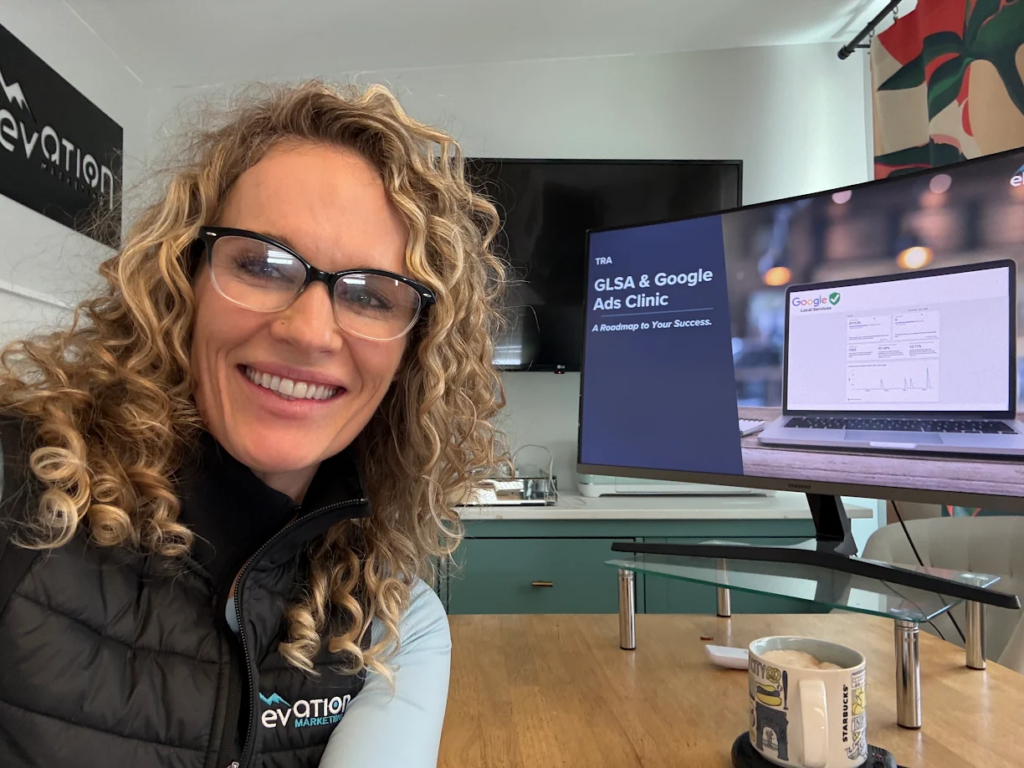 Amanda Joyce sitting at her desk smiling wearing her Elevation Marketing vest while working on a paid media presentation