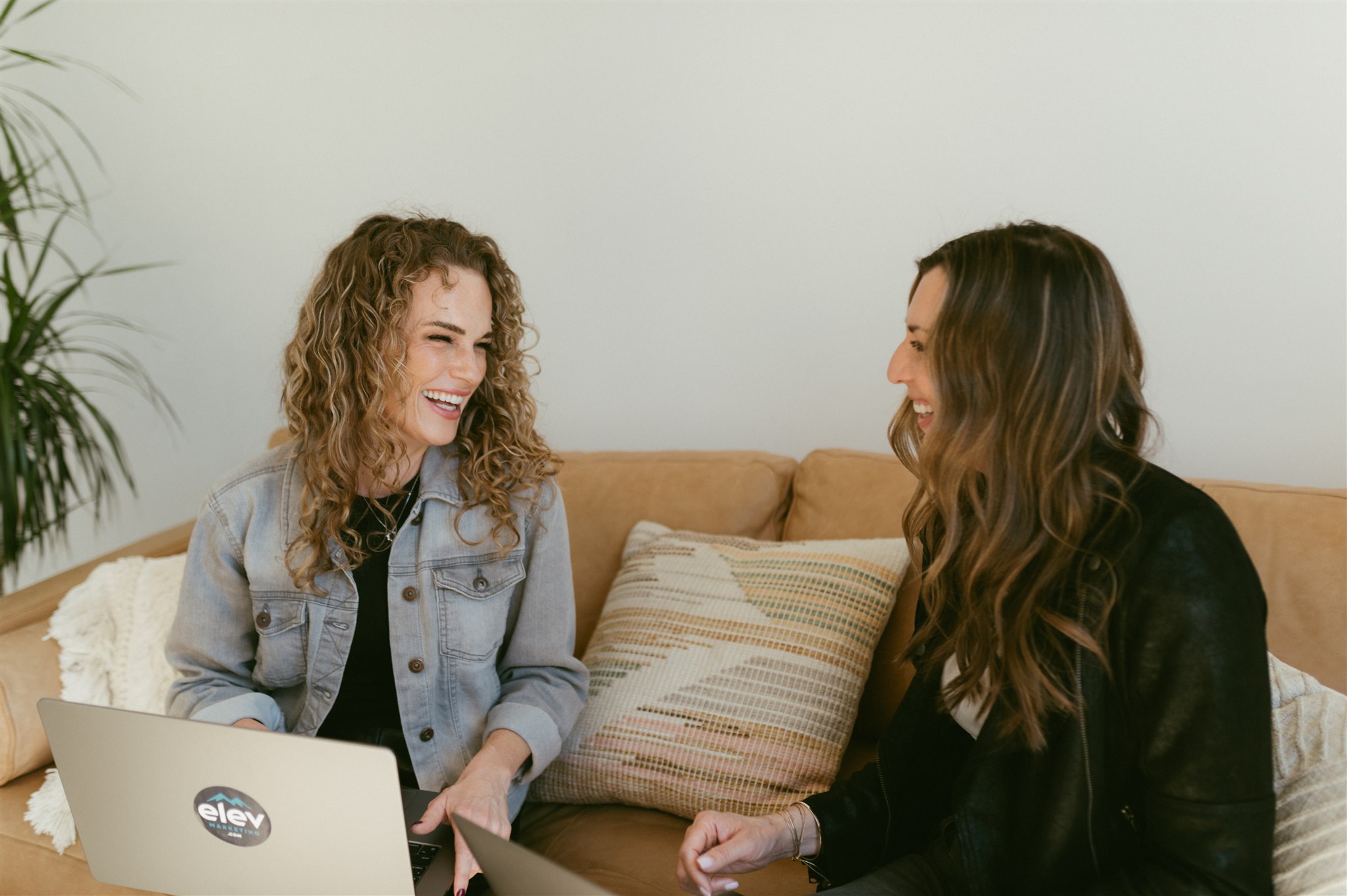 Two marketing strategists laughing while working on laptops to deliver fractional CMO for contractors fractional CMO services in Denver by Elevation Marketing
